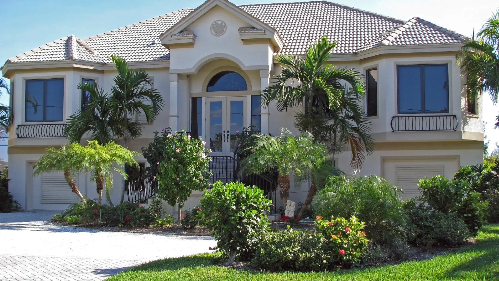 Elegant suburban home with lush landscaping and palm trees under a clear blue sky.