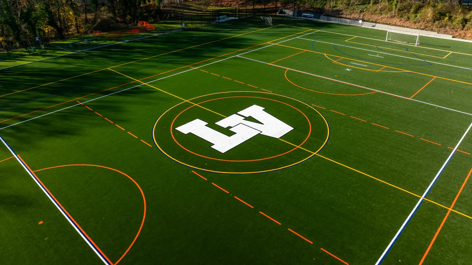 Aerial view of a green sports field with multiple colored lines and a large white 'A' logo in the center.