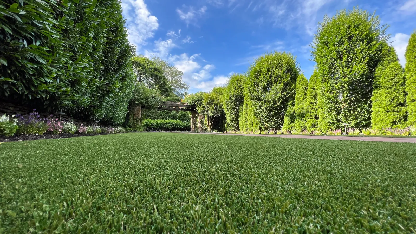 Lush green artificial grass surrounded by vibrant hedges under a clear blue sky.