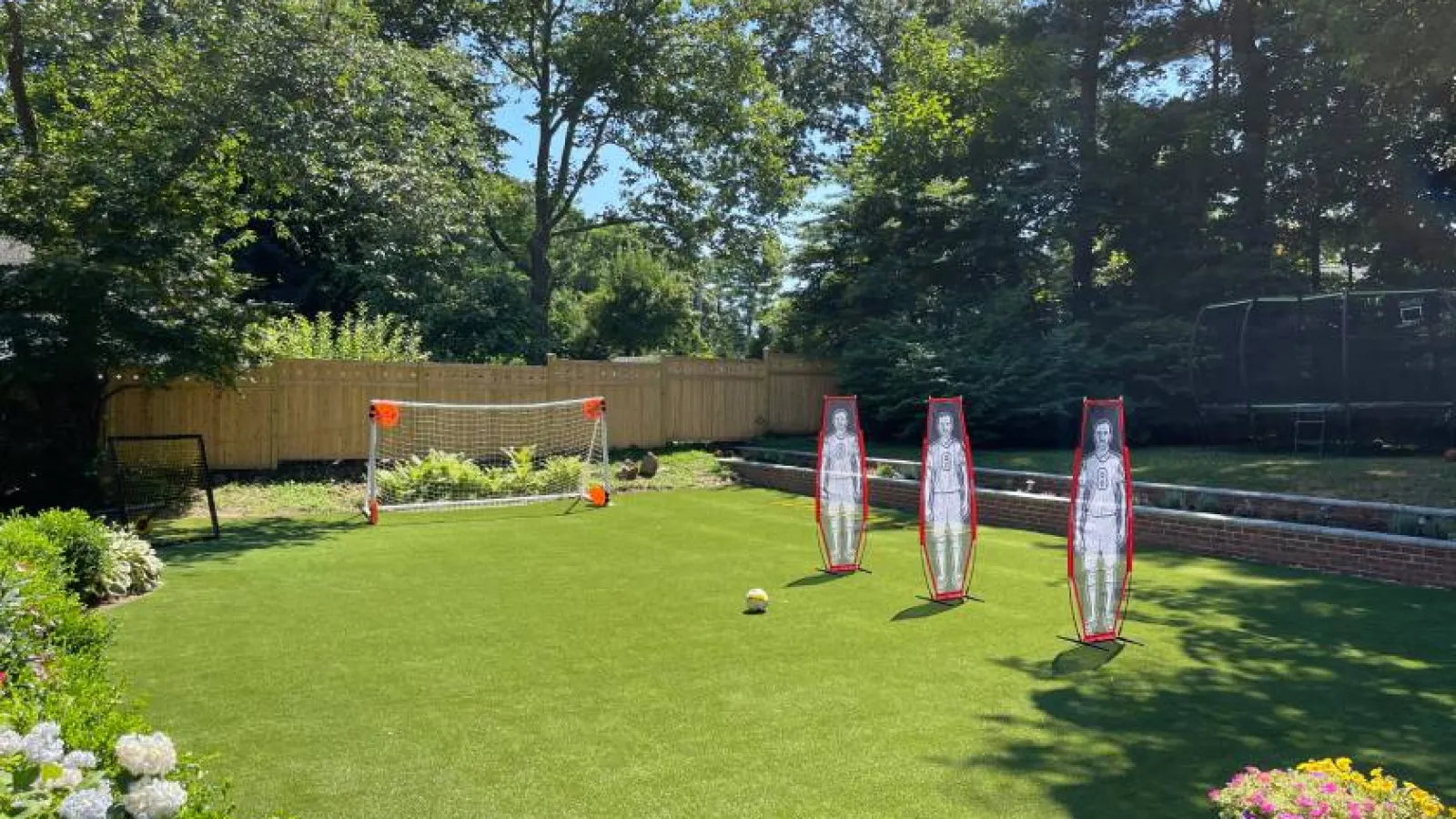 Backyard soccer practice setup with goal, three mannequin defenders, and soccer ball on green grass.