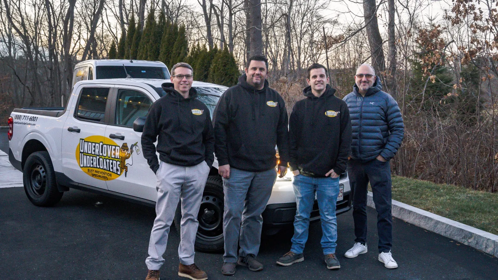 Four men standing beside a branded Undercover Underloaters pest control white pickup truck in a leafless wooded area