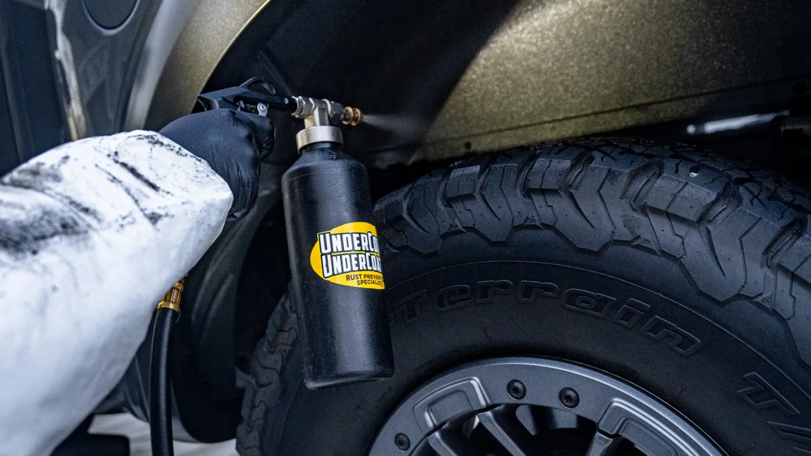 Person applying rust protection spray to Ford Shelby Raptor truck fender near tire in work environment