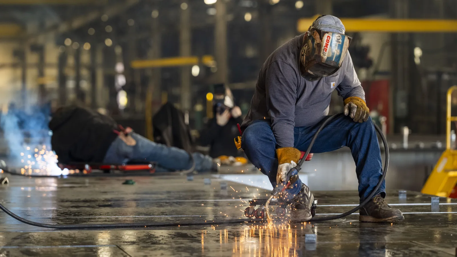 Welder cutting metal with sparks flying in an industrial workshop with workers in protective gear.