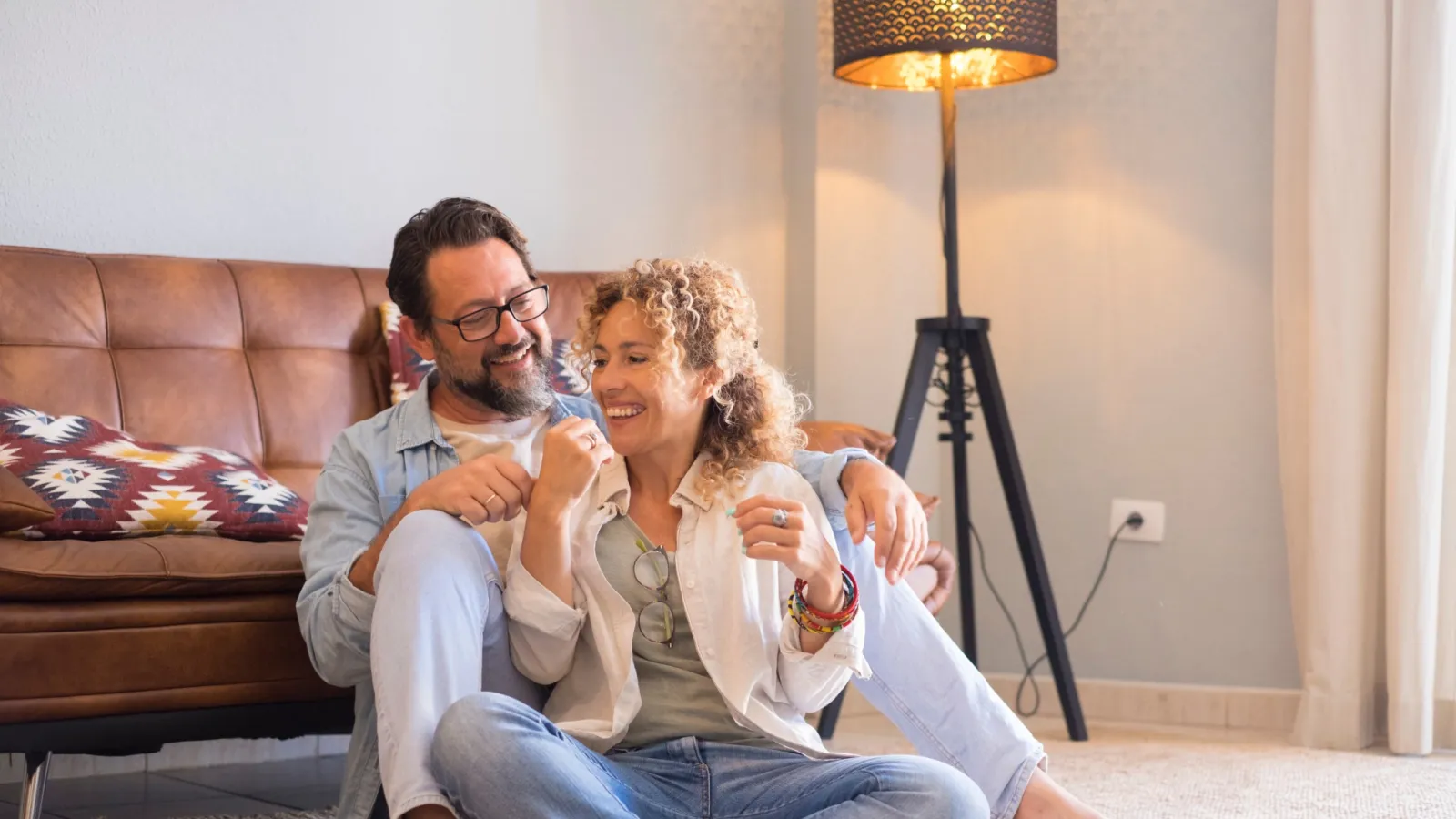 Couple sitting together on the floor, enjoying a cozy moment in a living room with stylish decor and warm lighting.