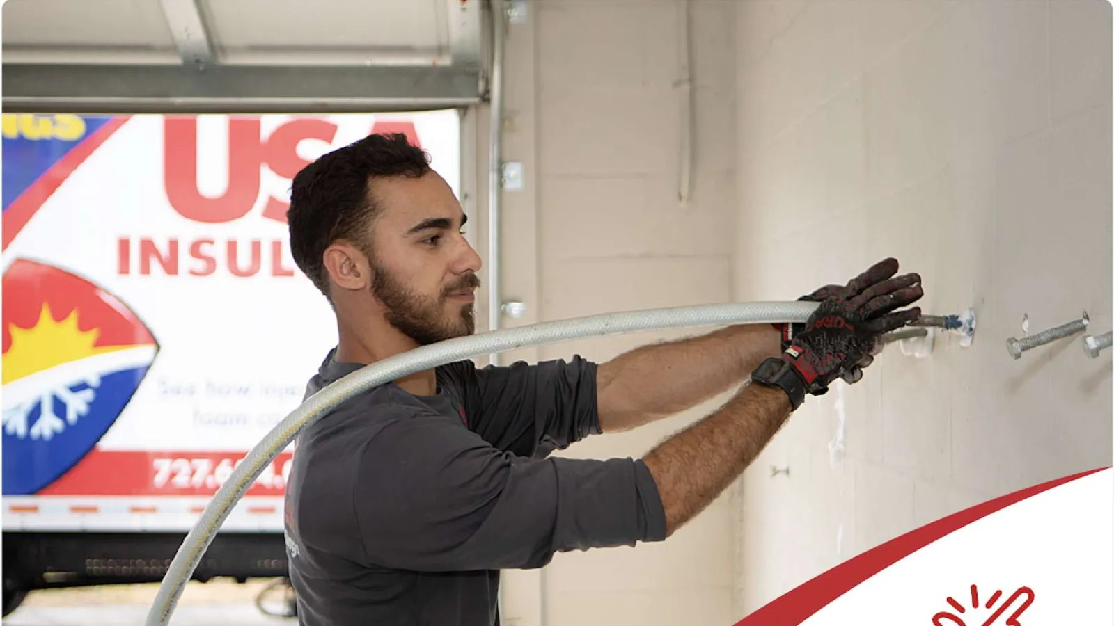 Worker installing insulation hose on wall in a garage setting with USA Insulation truck in background