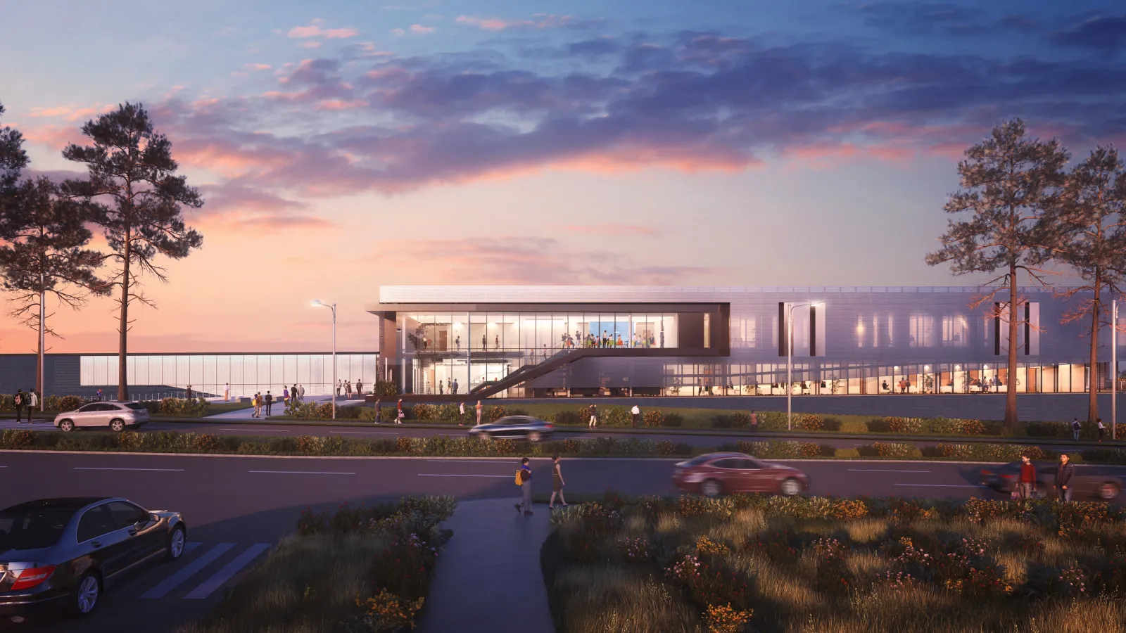 Modern glass building at sunset with cars and people near a roadside and tall trees around