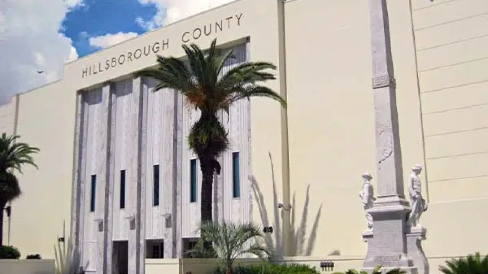 Hillsborough County government building with palm trees and a stone monument under a blue sky.