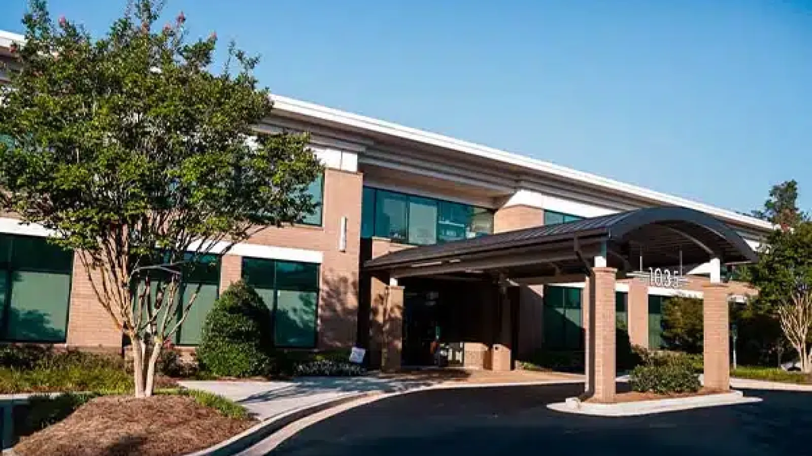 Modern two-story office building with brick facade, large windows, covered entrance, and landscaped greenery.