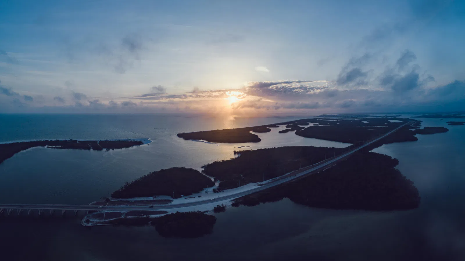 Aerial view of islands connected by bridges at sunset over calm ocean waters under a blue sky.