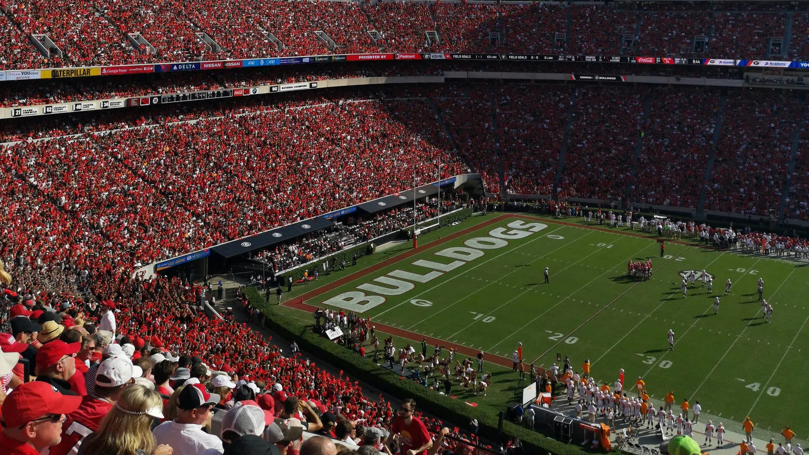 Crowded stadium with fans dressed in red watching a football game on a sunny day with ‘BULLDOGS’ on the field.