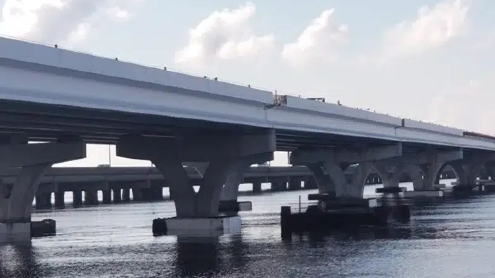 Concrete highway bridge with large supporting pillars over calm water under a partly cloudy sky