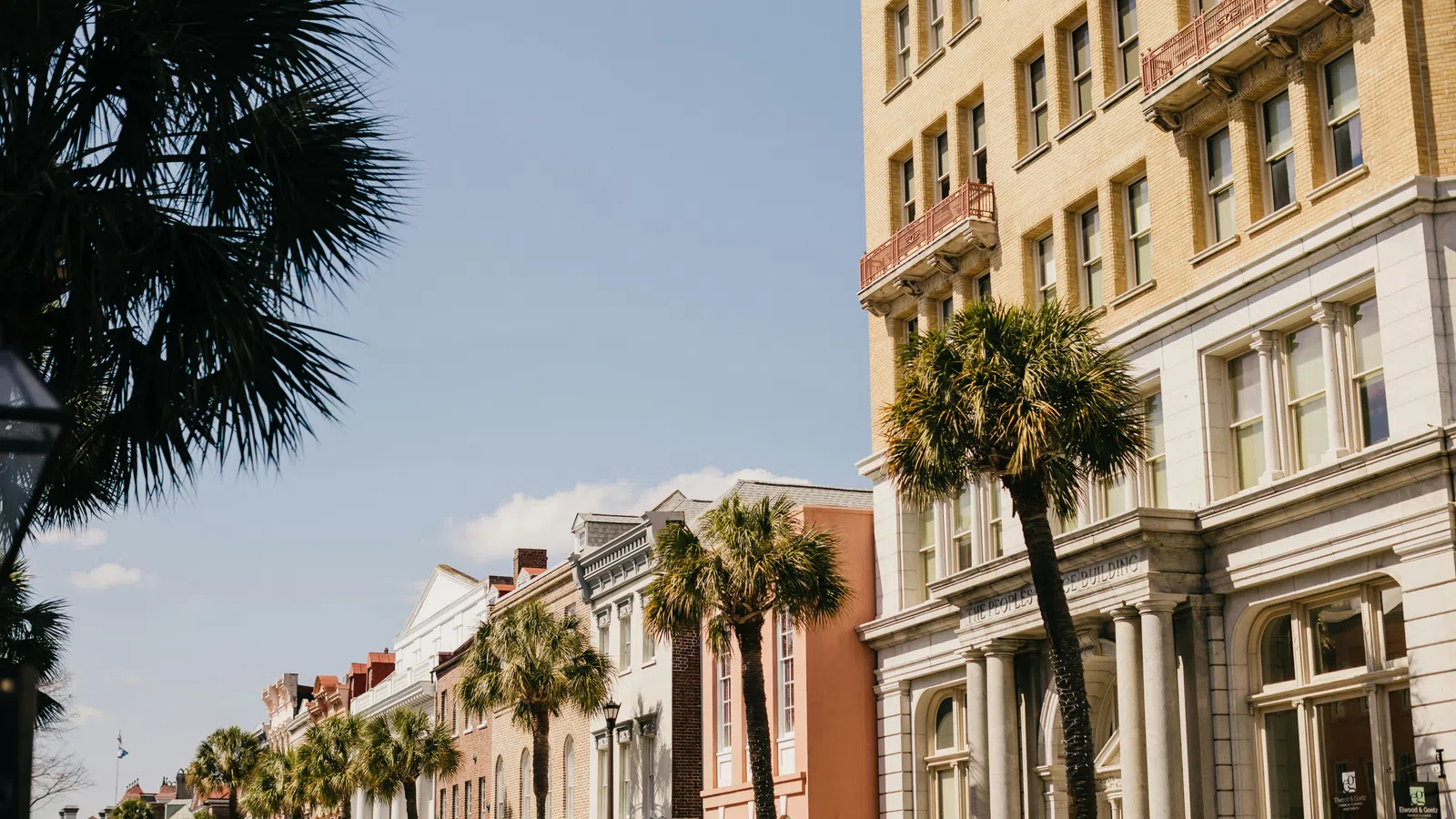 Row of historic buildings and palm trees lining a sunny street under clear blue sky