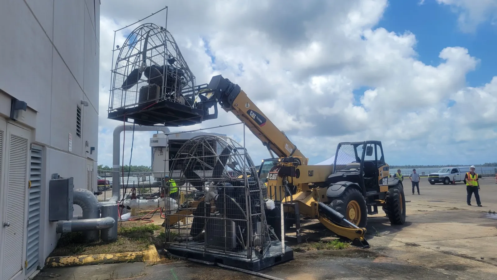 Construction site with a CAT telescopic handler lifting metal framework structures under a partly cloudy sky.