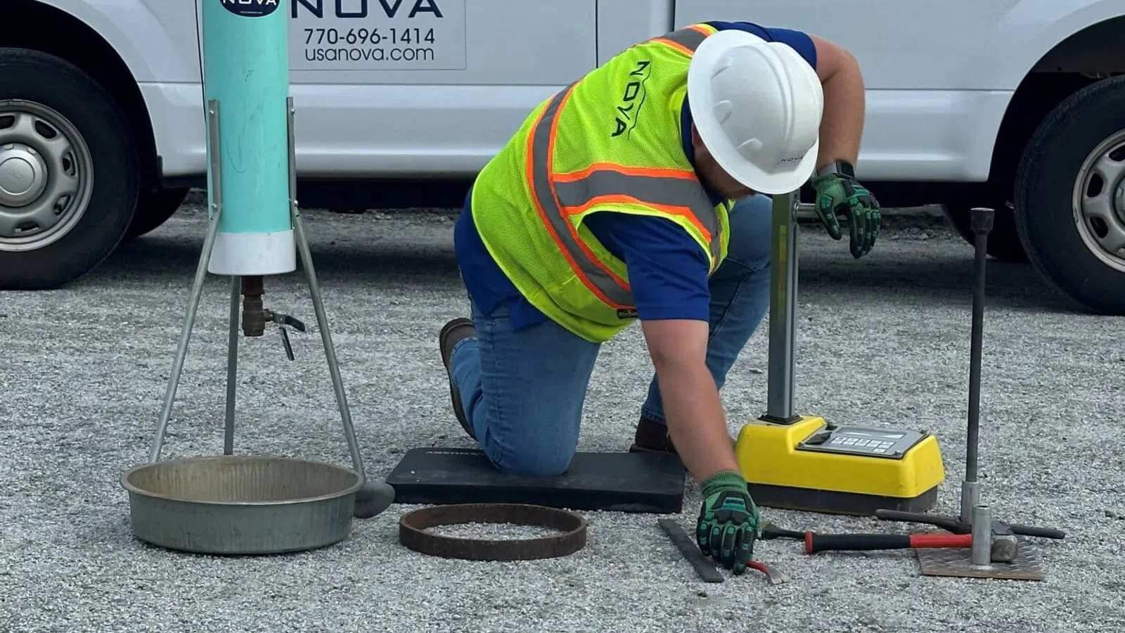 Construction worker in safety gear testing gravel compaction near Nova company truck outdoors.