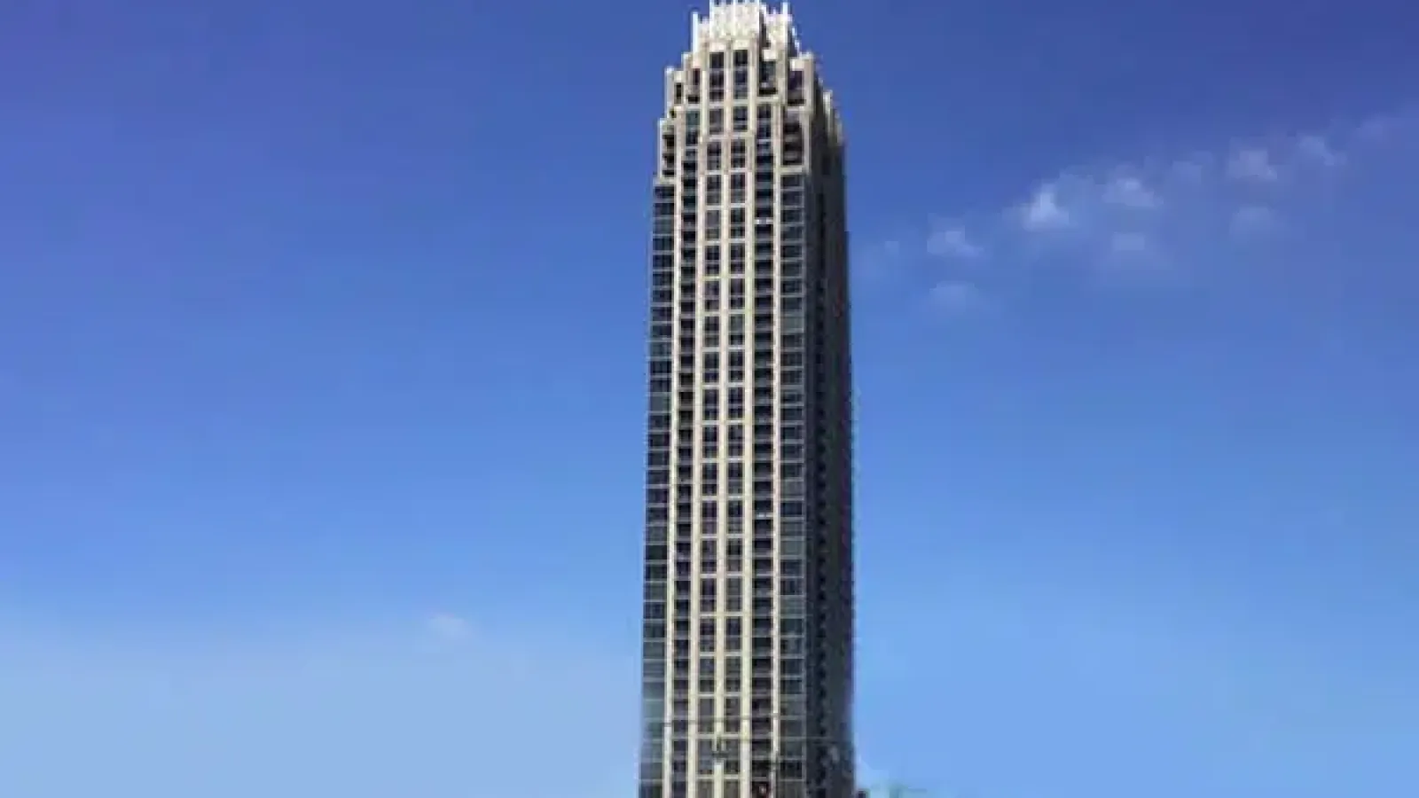 Tall modern skyscraper with intricate crown detail against a clear blue sky on a sunny day