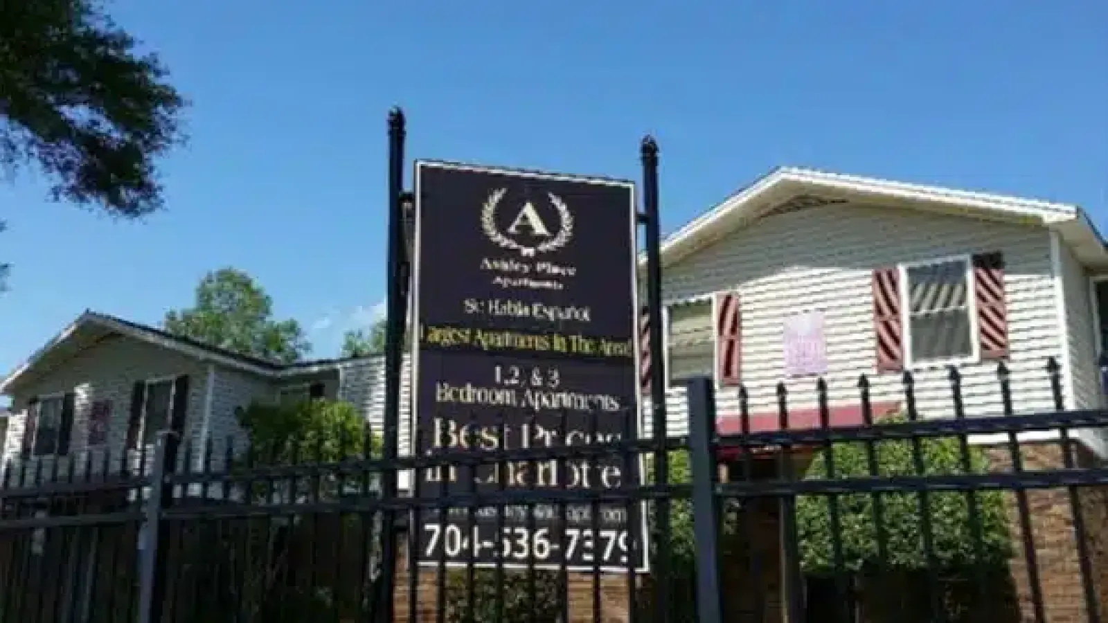 Ashley Place Apartments sign advertising 1 to 3 bedroom apartments behind a black iron fence under a clear blue sky.