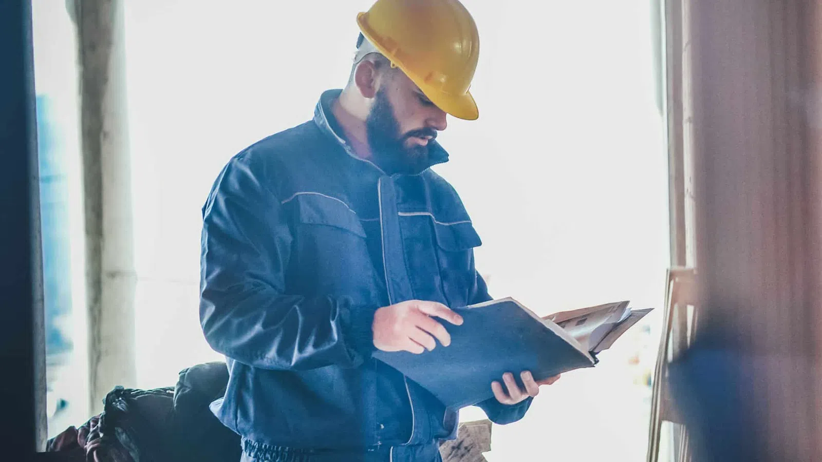 Construction worker wearing a yellow hard hat reading documents inside a building under construction