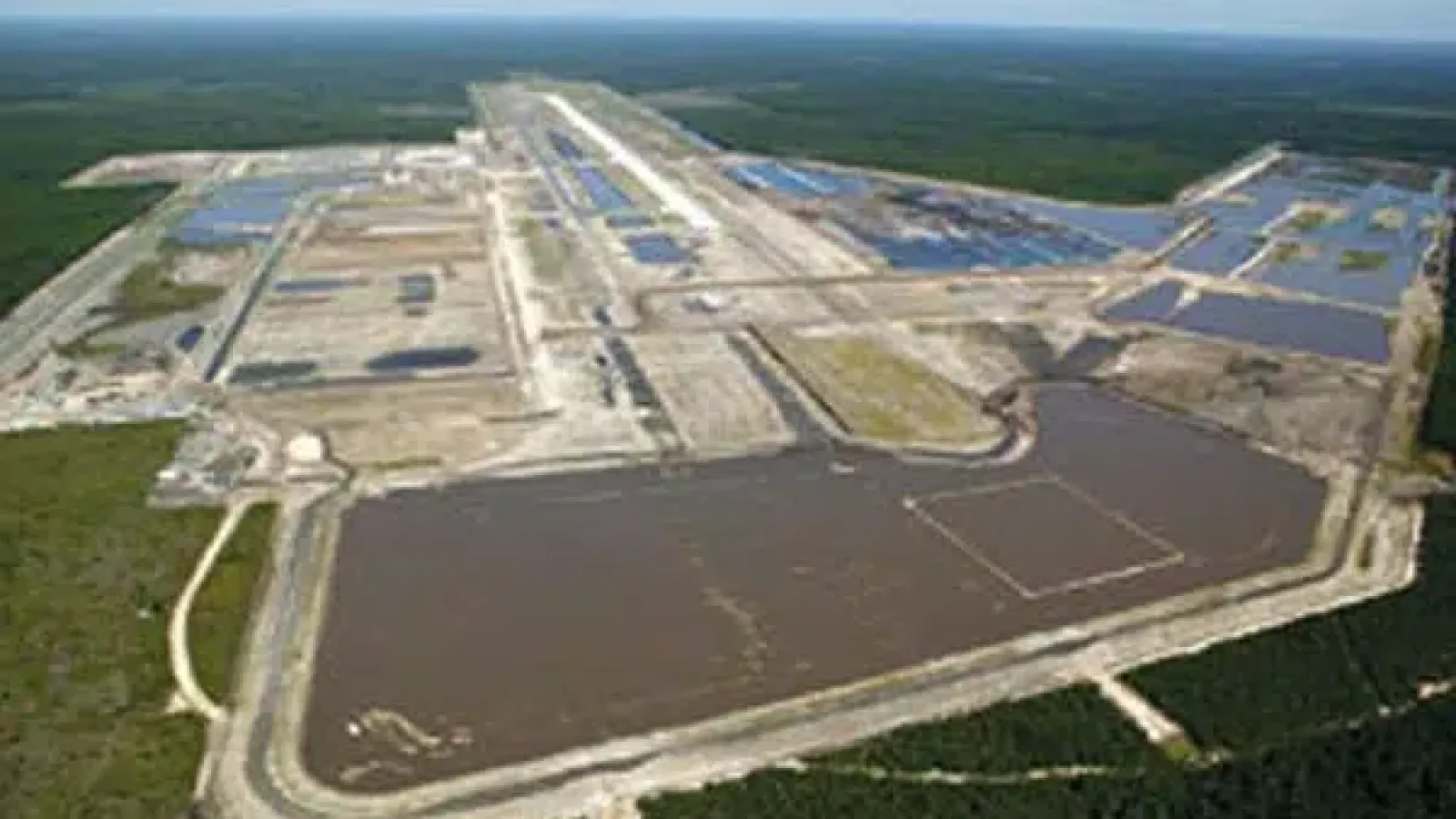 Aerial view of large evaporation ponds with surrounding roads and forested area in the background.