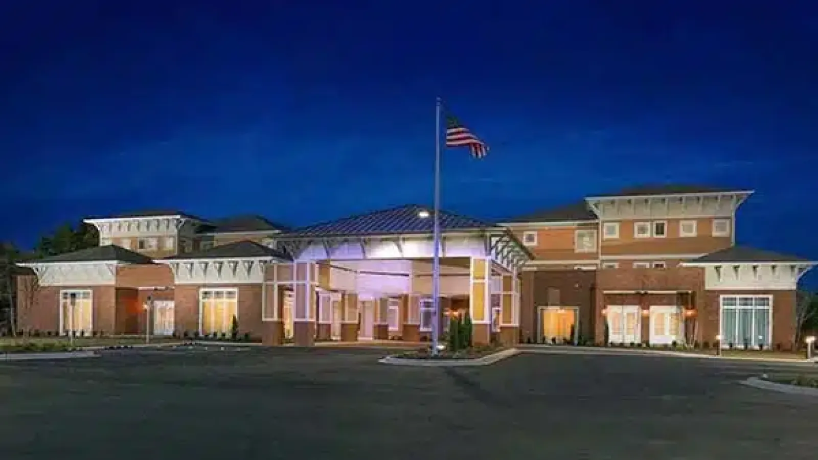 Night view of a large modern brick building with an American flag in front and illuminated entrance driveway.