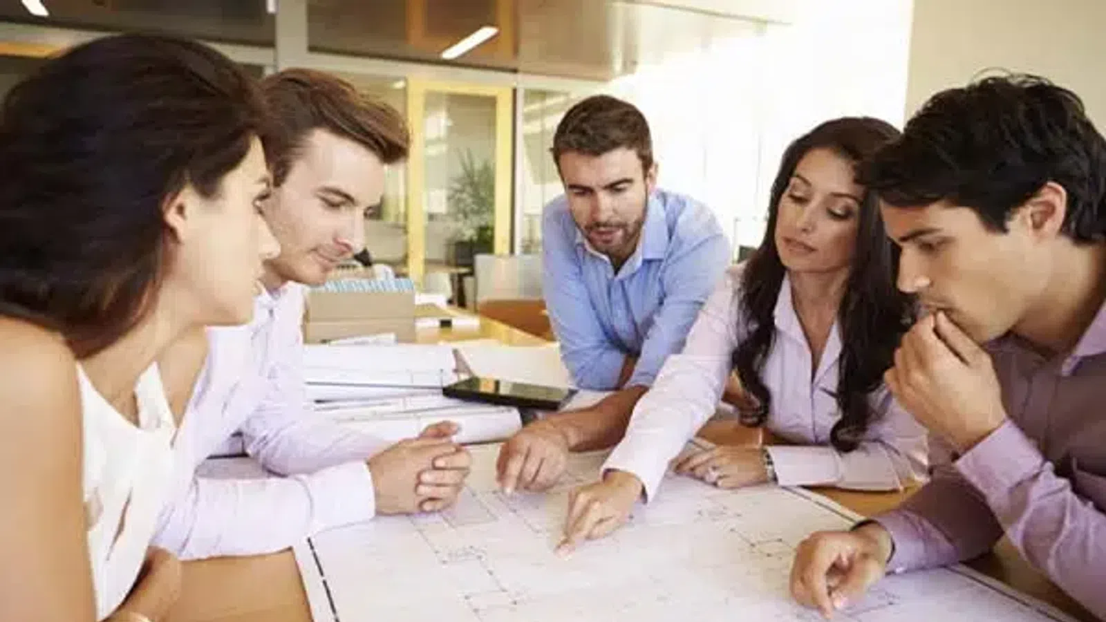 Team of professionals collaborating and discussing architectural blueprints in a modern office setting.