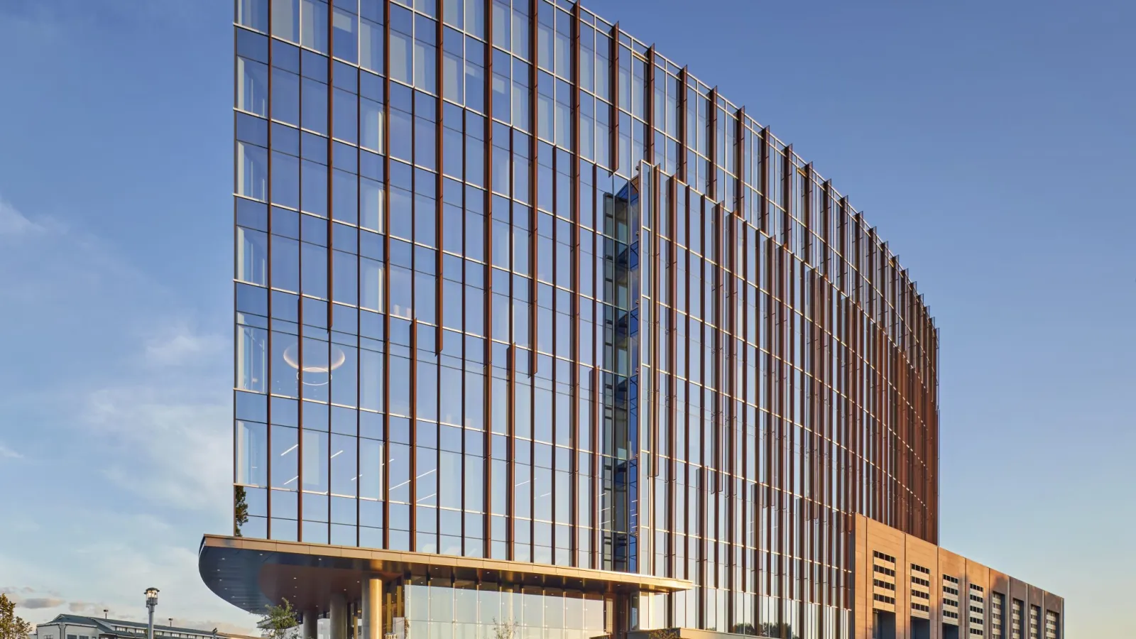 Modern curved office building with glass facade reflecting clear sky and busy street traffic in foreground