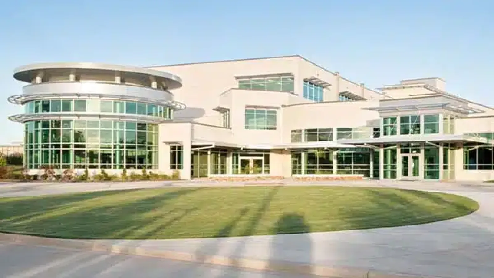 Modern commercial building with large glass windows surrounded by green lawn and clear blue sky.