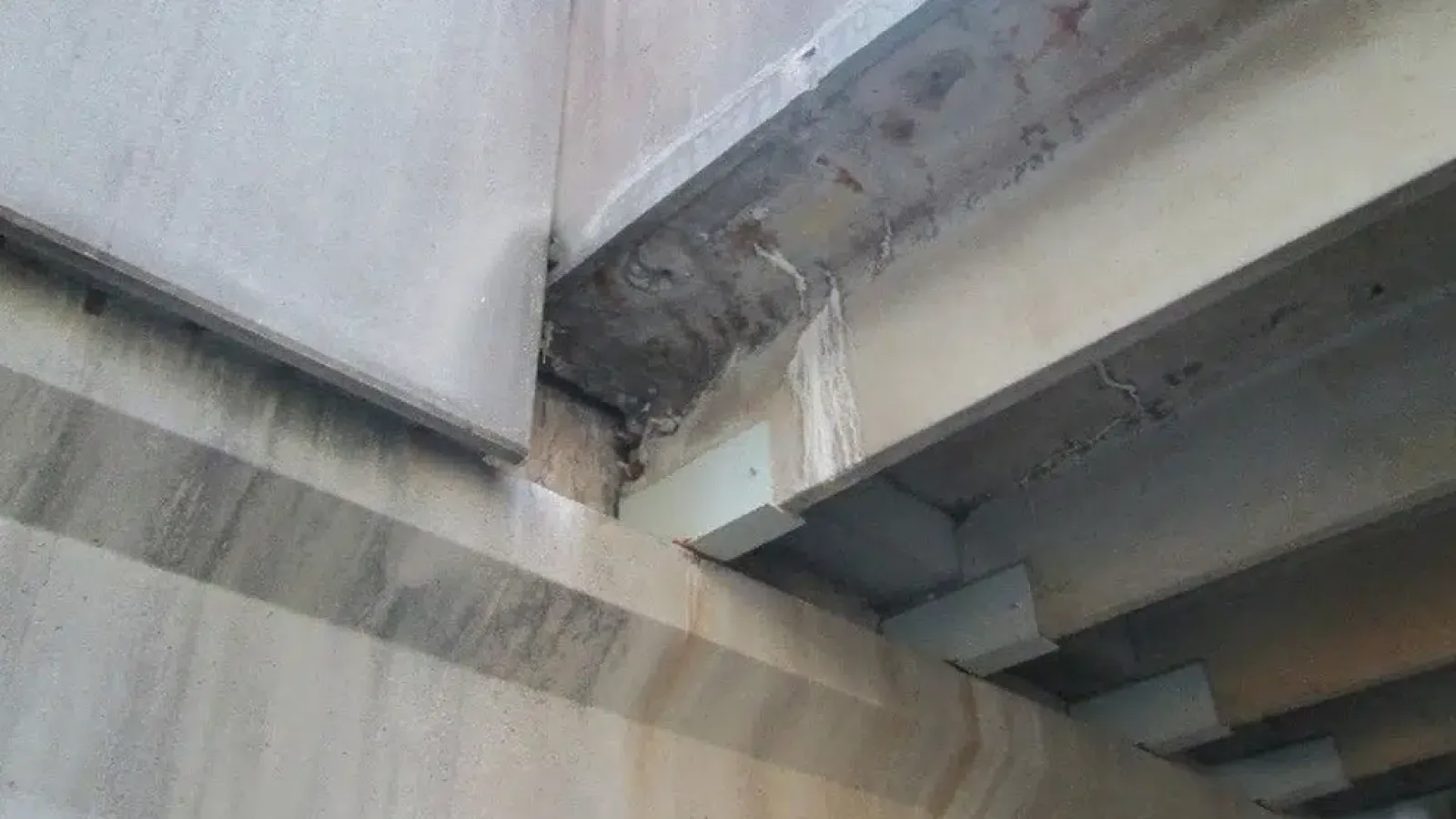 Close-up of concrete structure with water leakage and stains on bridge or building beams under repair.