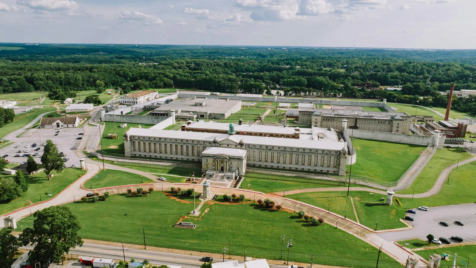 Aerial view of a large historic prison complex surrounded by green lawns and trees under a blue sky.
