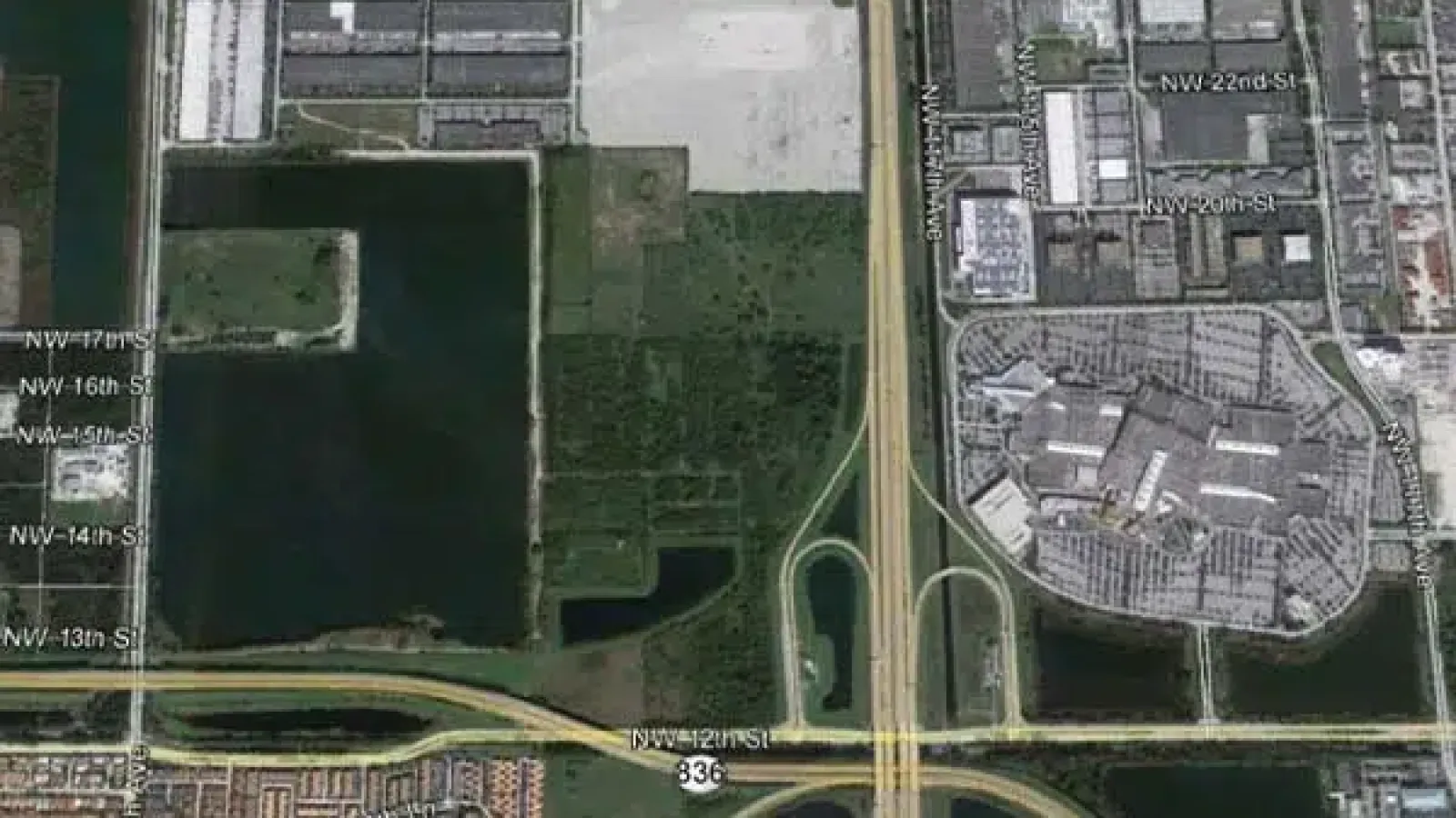 Aerial view of a highway interchange near commercial and residential areas with water bodies and green spaces.