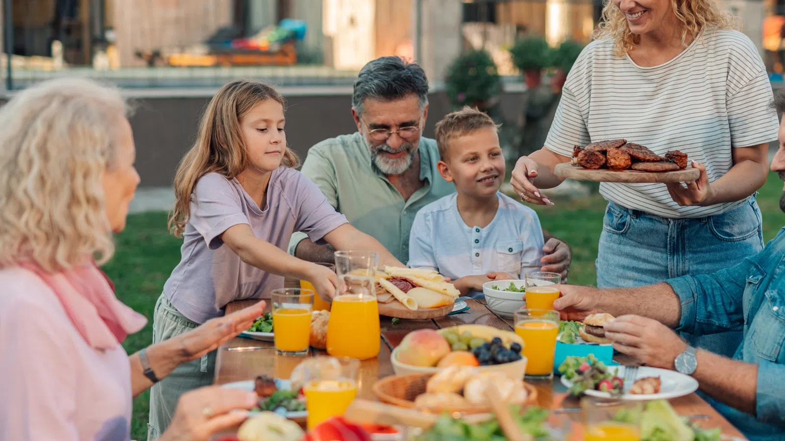 Family enjoying a meal together outdoors with fresh food and orange juice on a sunny day.