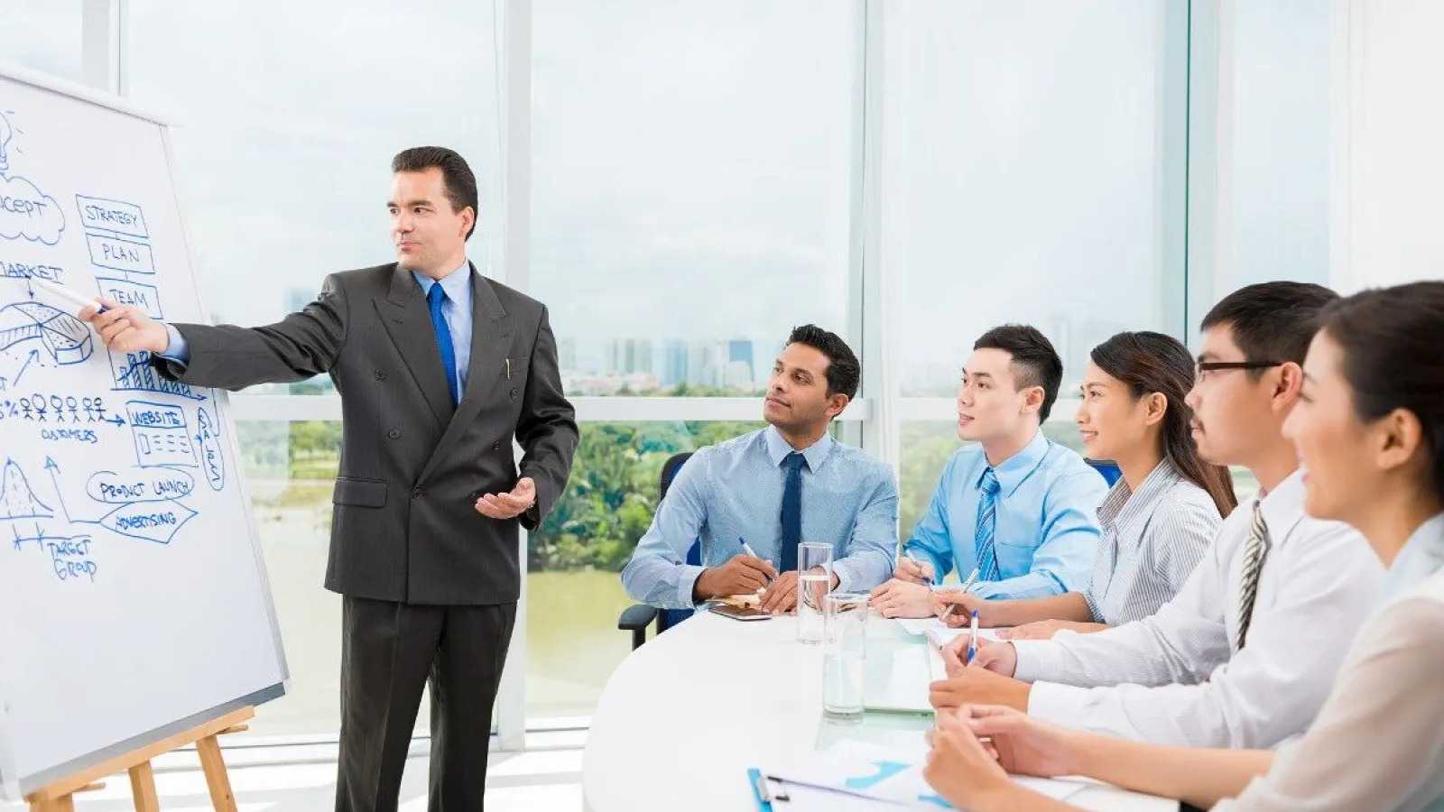 Businessman presenting strategy and marketing plan on whiteboard to attentive team in modern office