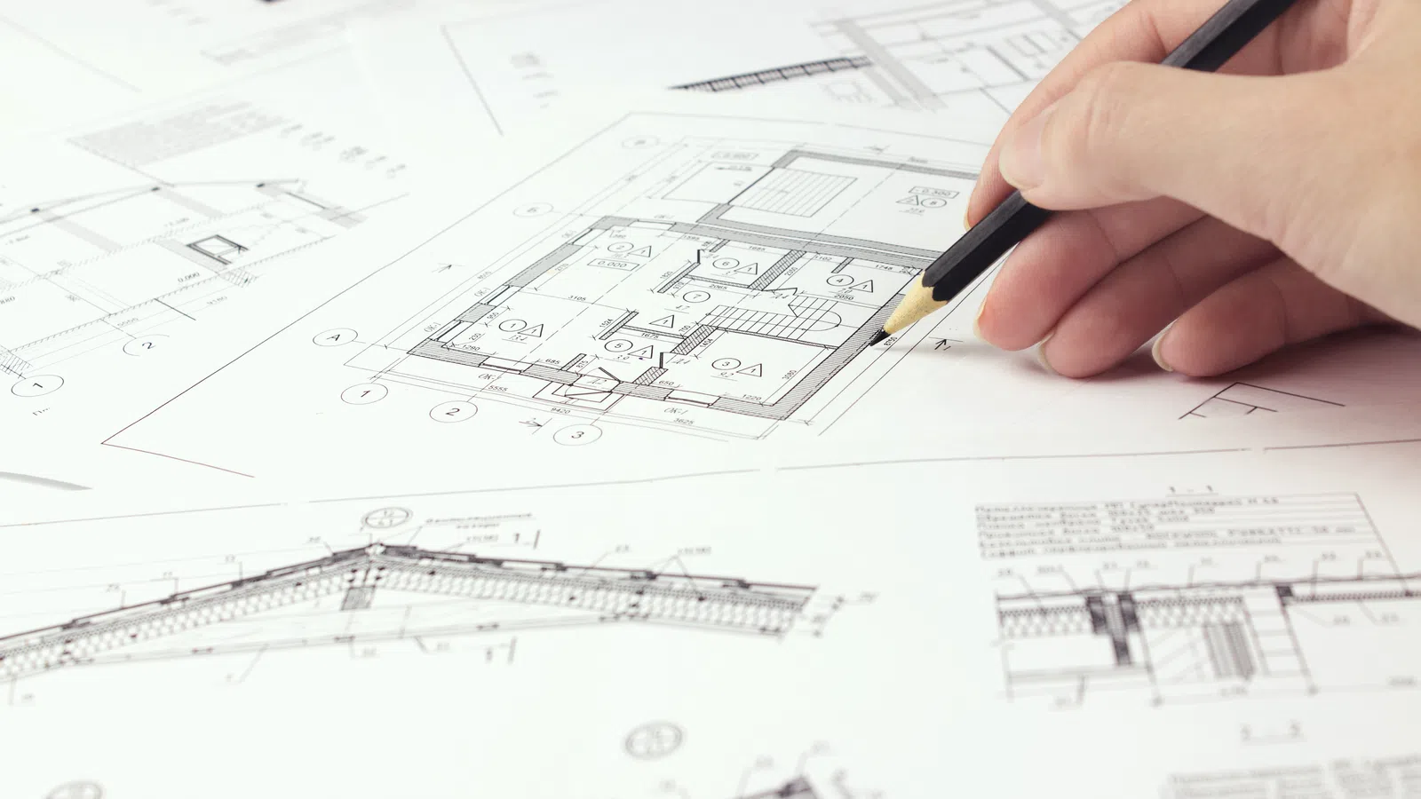 Hand drawing and reviewing architectural floor plans and blueprints with pencil on paper for construction design.