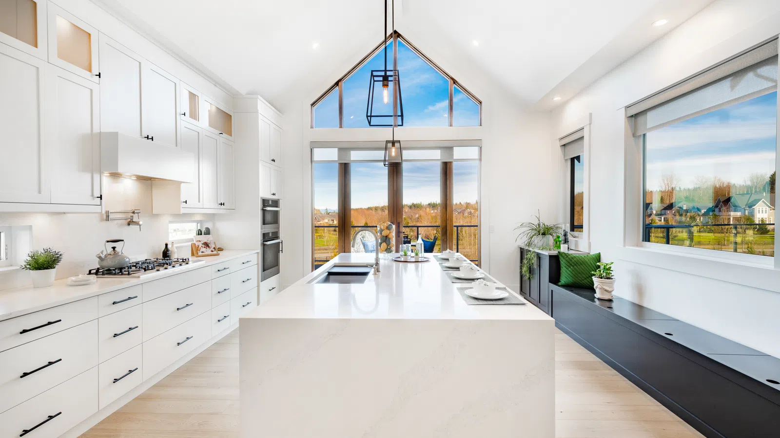 Bright modern kitchen with white cabinetry, large island, and floor-to-ceiling windows overlooking scenic landscape.