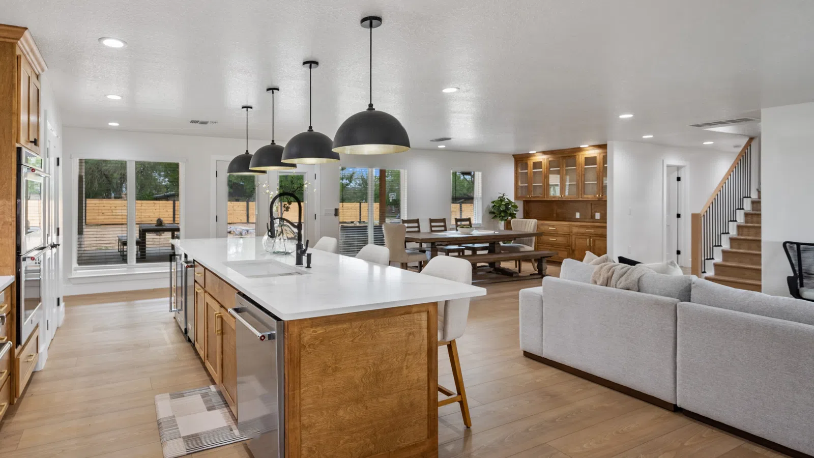 Spacious open-plan kitchen and living area with wooden cabinetry, white island, modern lighting, and dining space