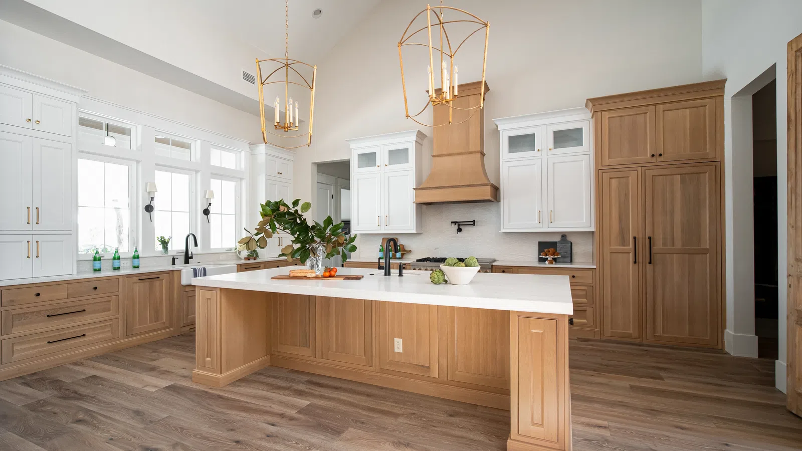 Spacious modern kitchen with wood cabinetry, large island, white countertops, and hanging gold light fixtures.