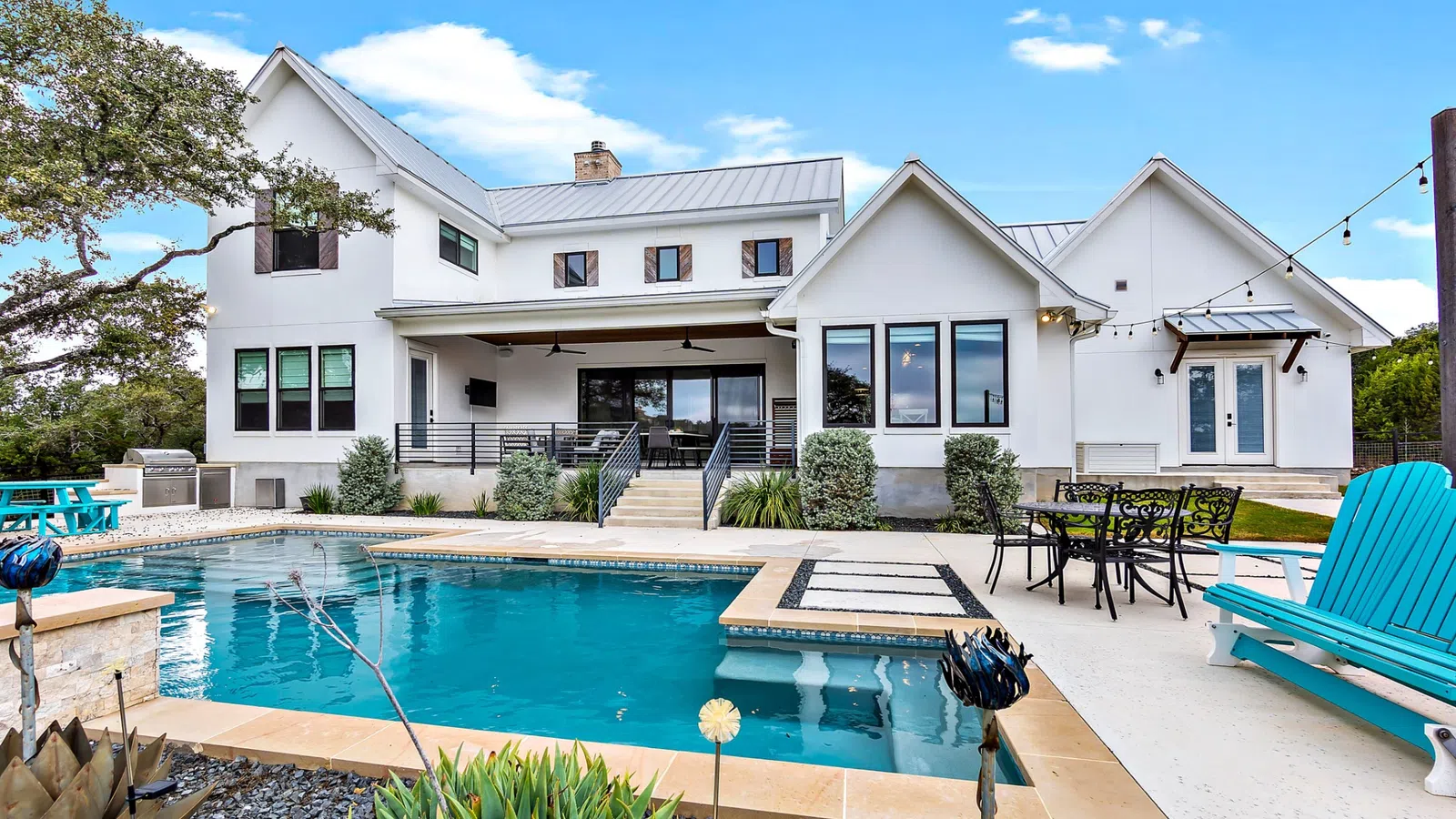 Modern white house with large windows overlooks a private backyard pool and outdoor seating area under clear skies