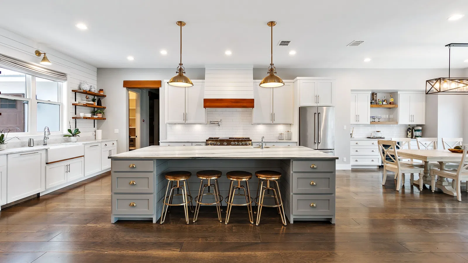 Spacious modern kitchen with large island, wooden stools, white cabinetry, hardwood floors, and pendant lighting.