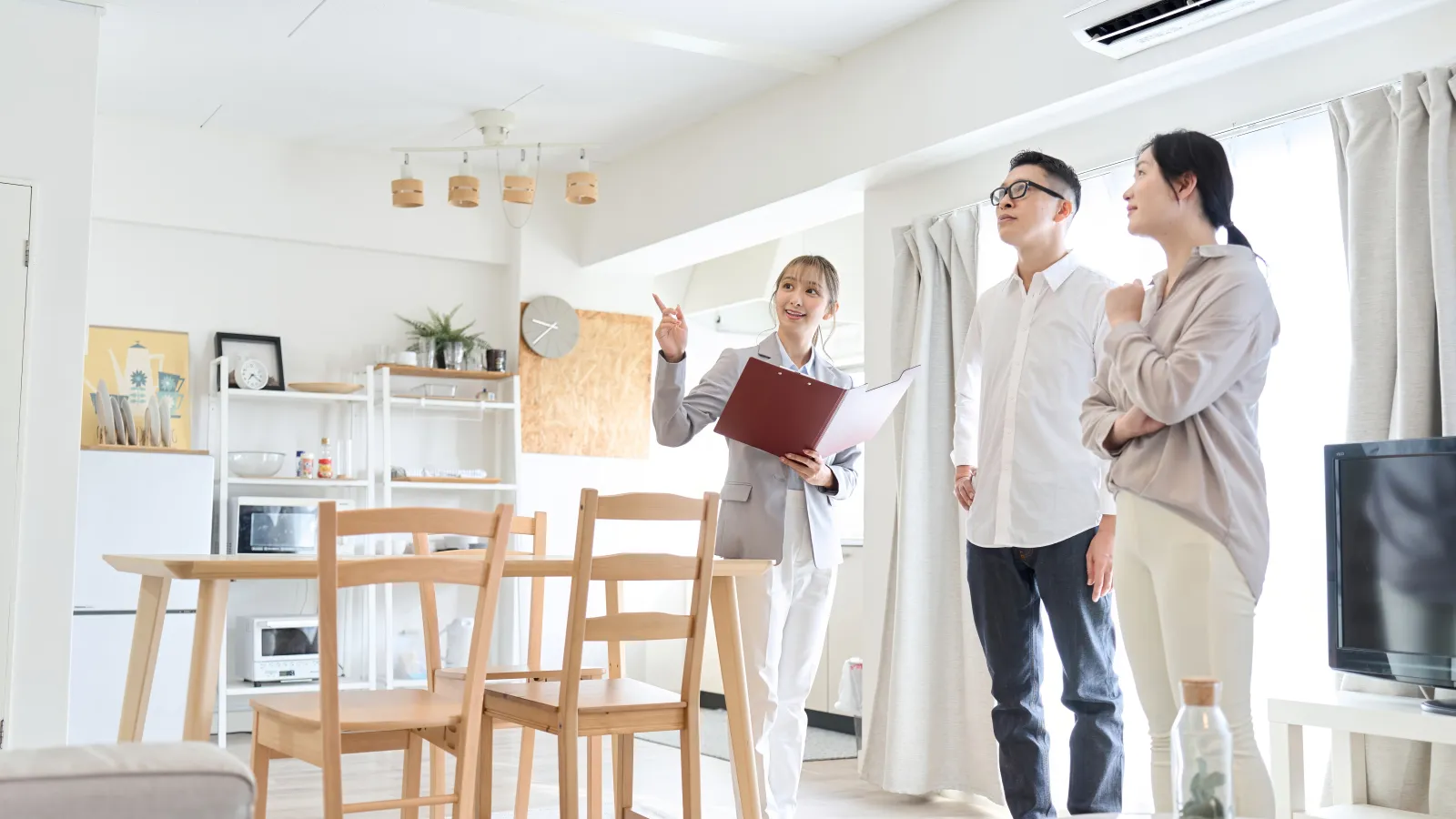 Real estate agent showing a couple a modern, bright apartment with wooden furniture and white decor.