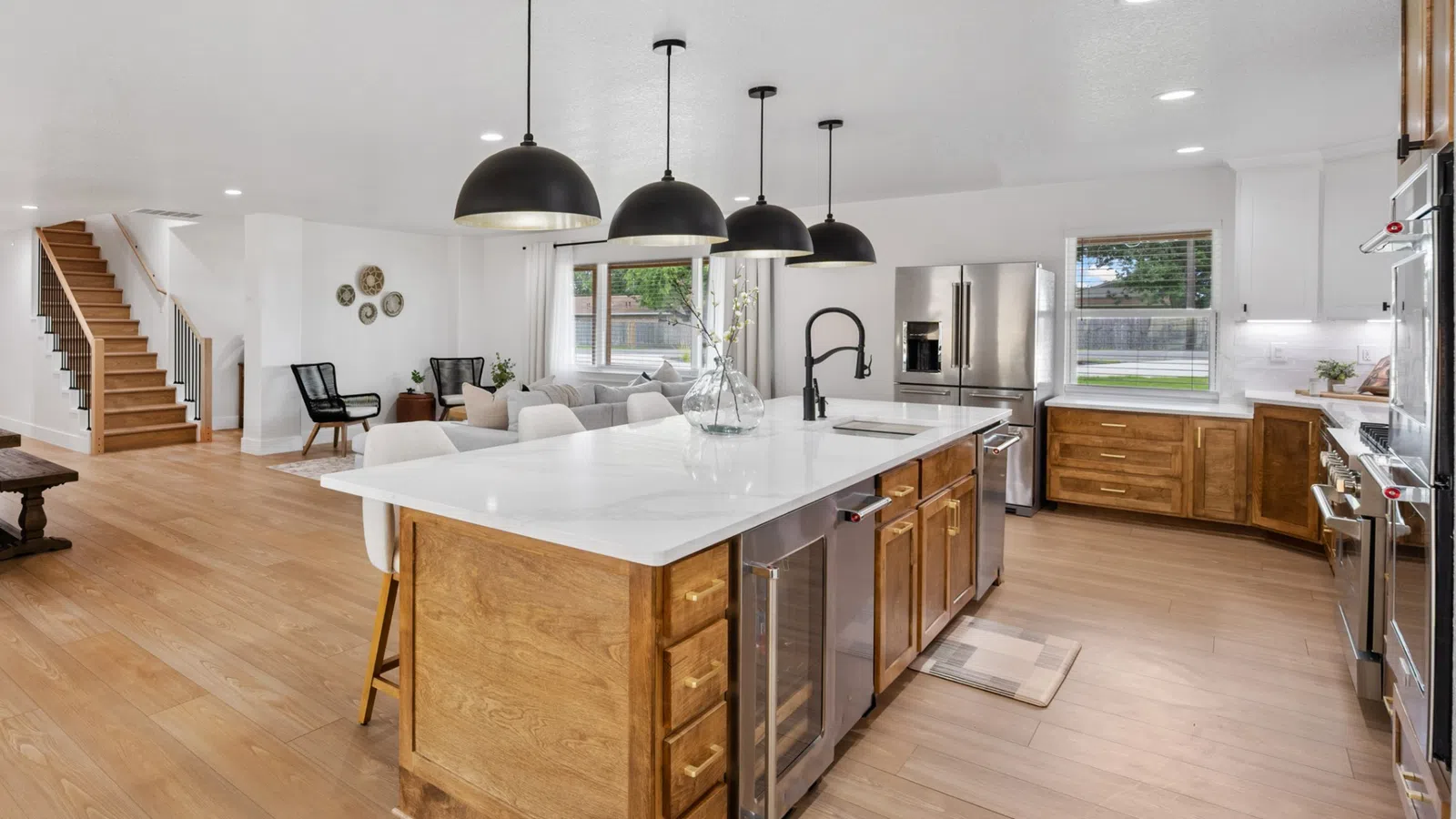 Modern open kitchen with large white island, wooden cabinets, stainless steel appliances, and black pendant lights