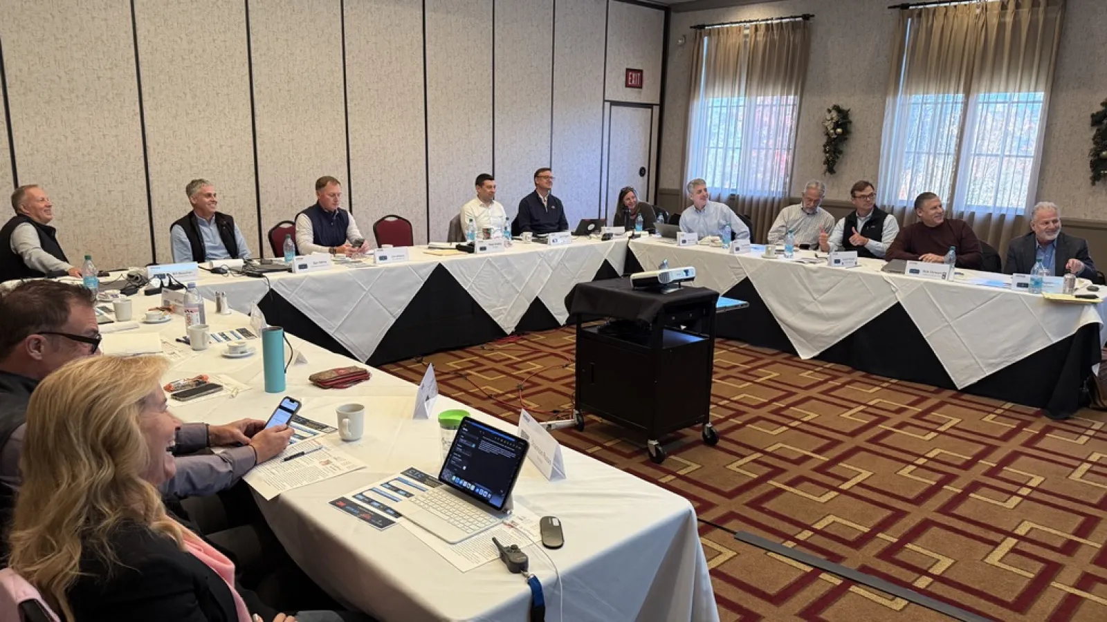 Business meeting with people seated around a U-shaped table in a conference room with laptops and documents.