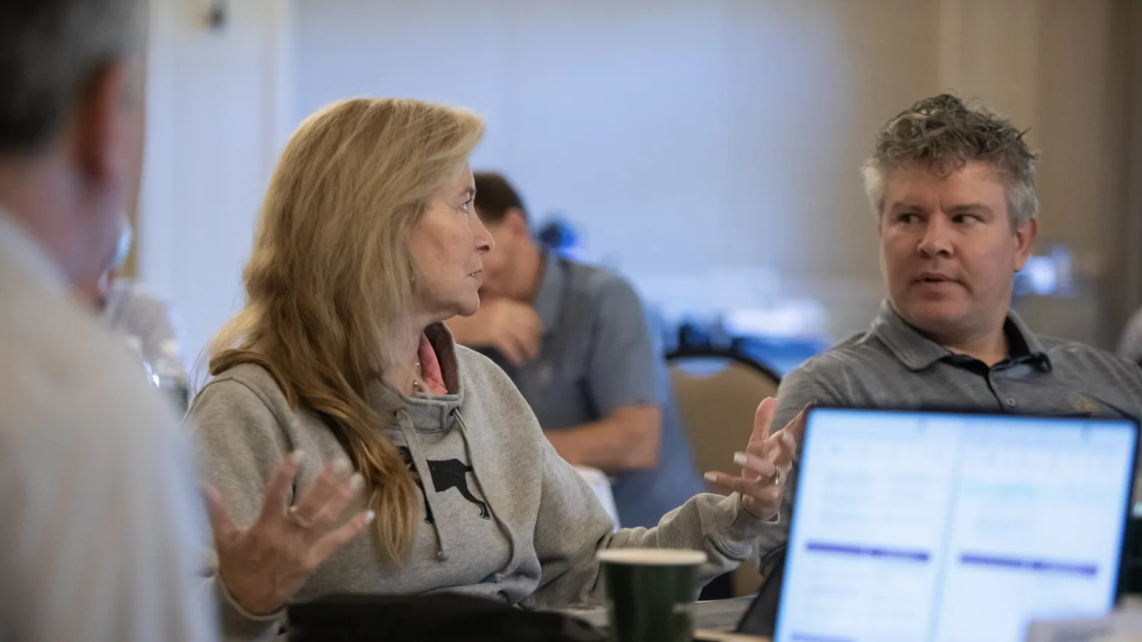Two colleagues in casual clothing discussing ideas during a meeting with laptop and coffee cup on the table