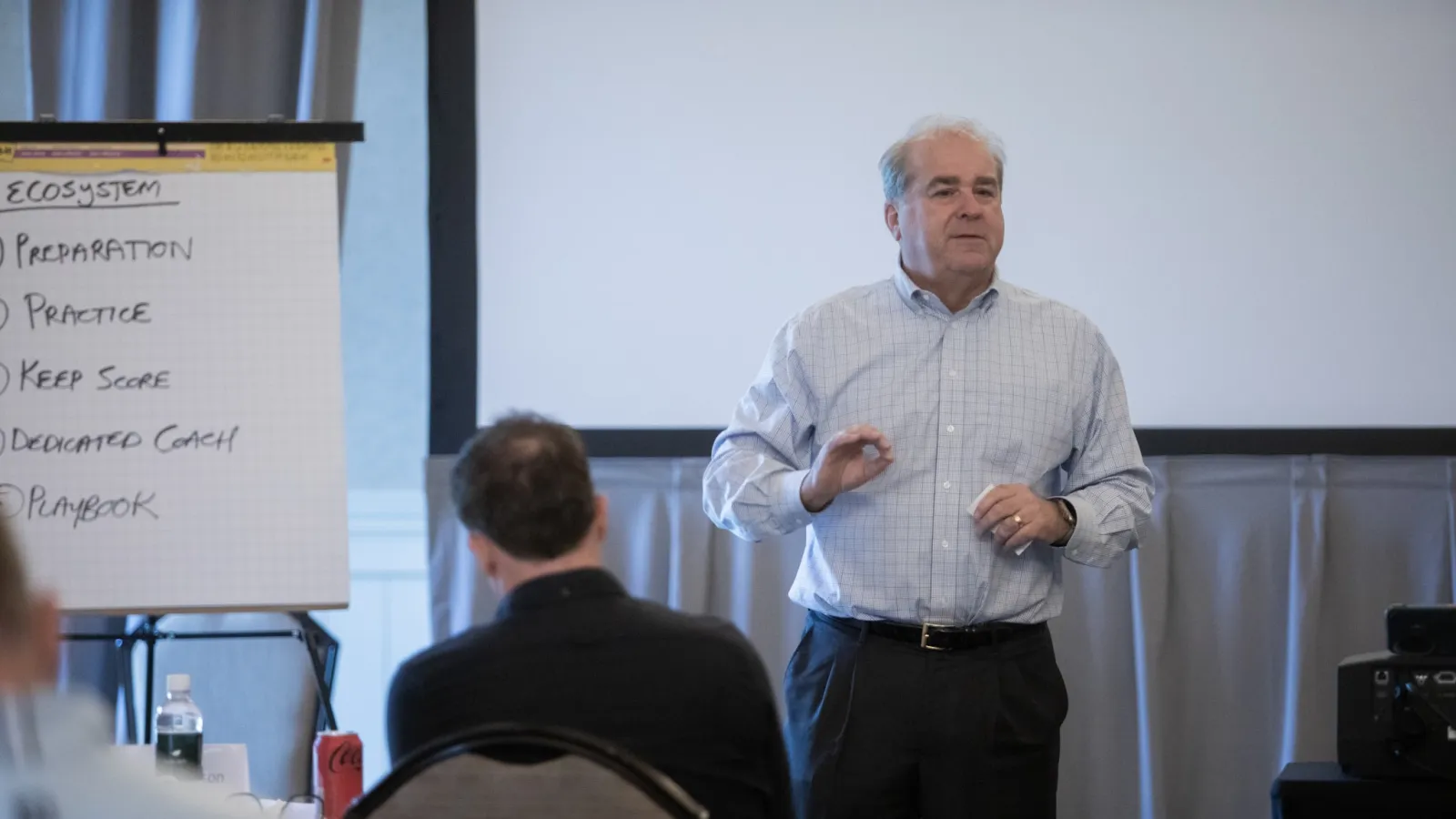 Businessman giving a presentation to an audience with a flip chart listing ecosystem steps in a conference room.
