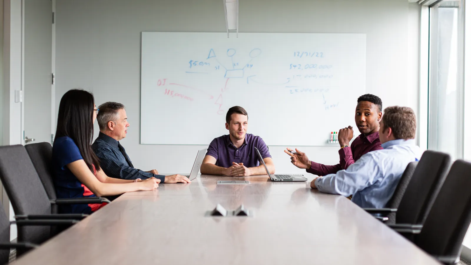a group of people sitting around a table in front of a whiteboard