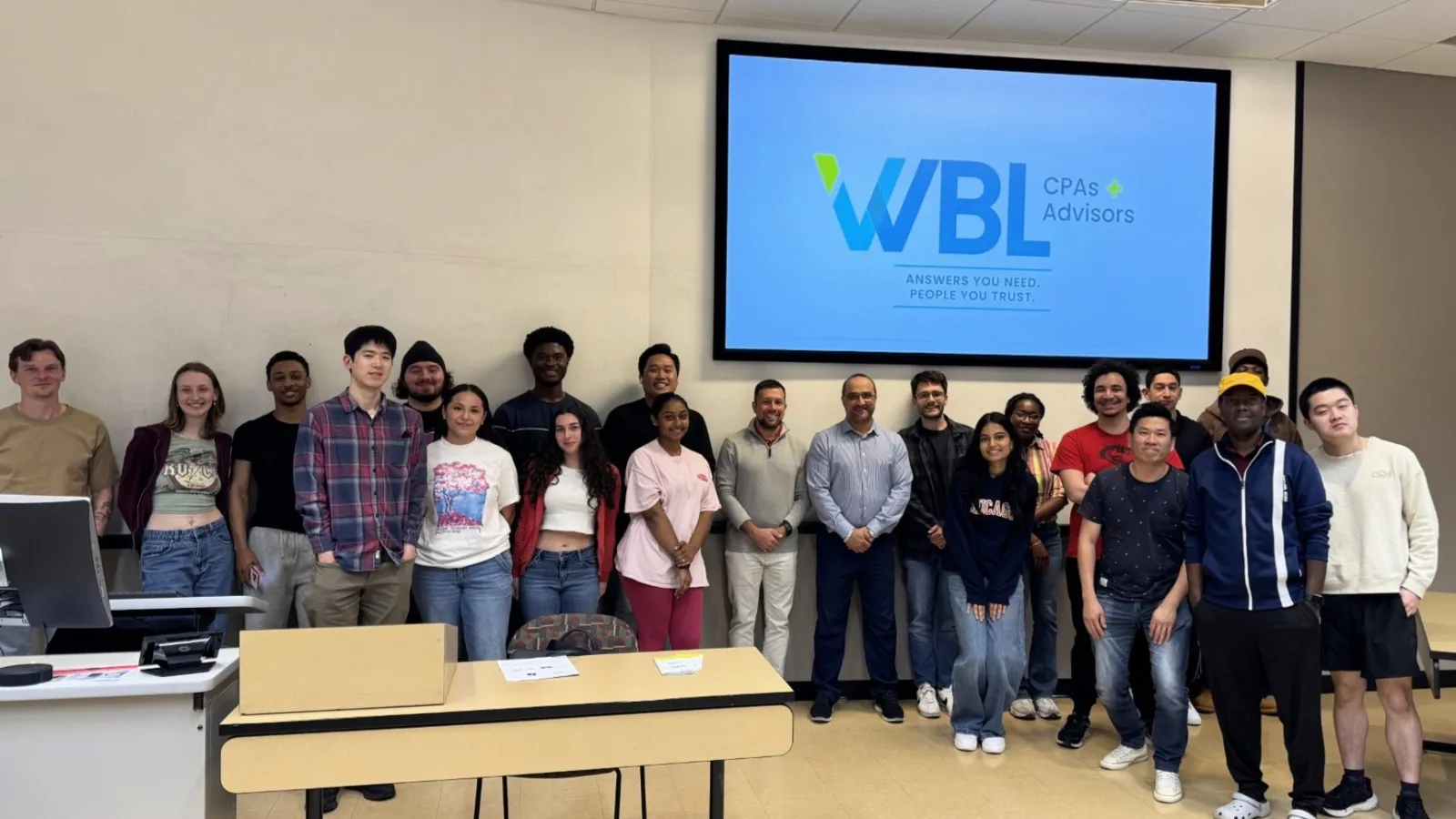 Diverse group of professionals standing in conference room with WBL CPAs Advisors logo on screen behind.