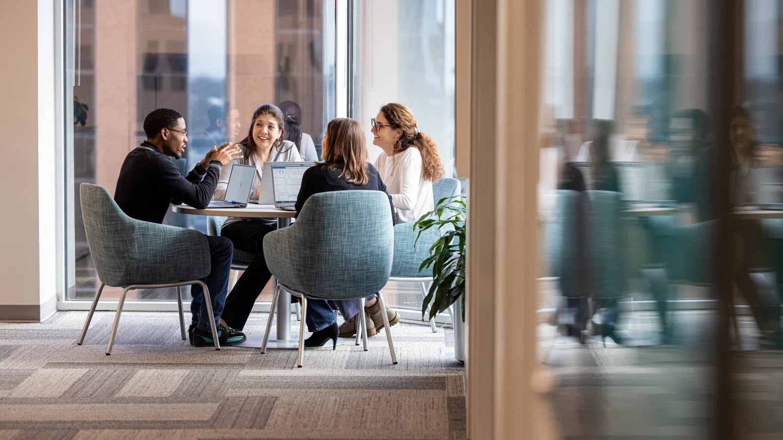 Group of professionals collaborating at a round table in a modern office space with large windows.