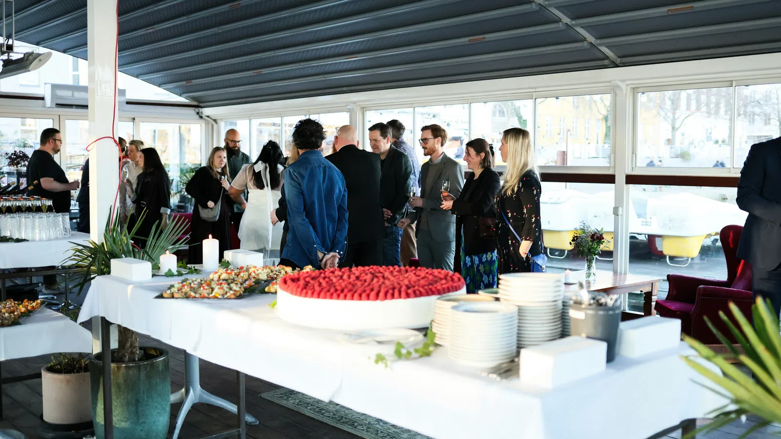 Guests socialize and enjoy refreshments at a modern indoor event with a buffet table featuring desserts and plates.