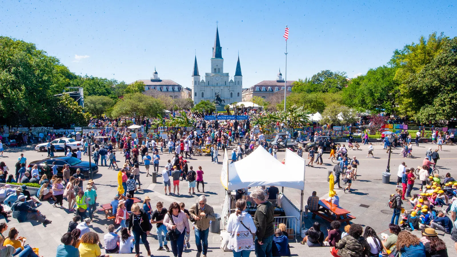 Crowd gathered at a lively outdoor event with St. Louis Cathedral in the background on a sunny day