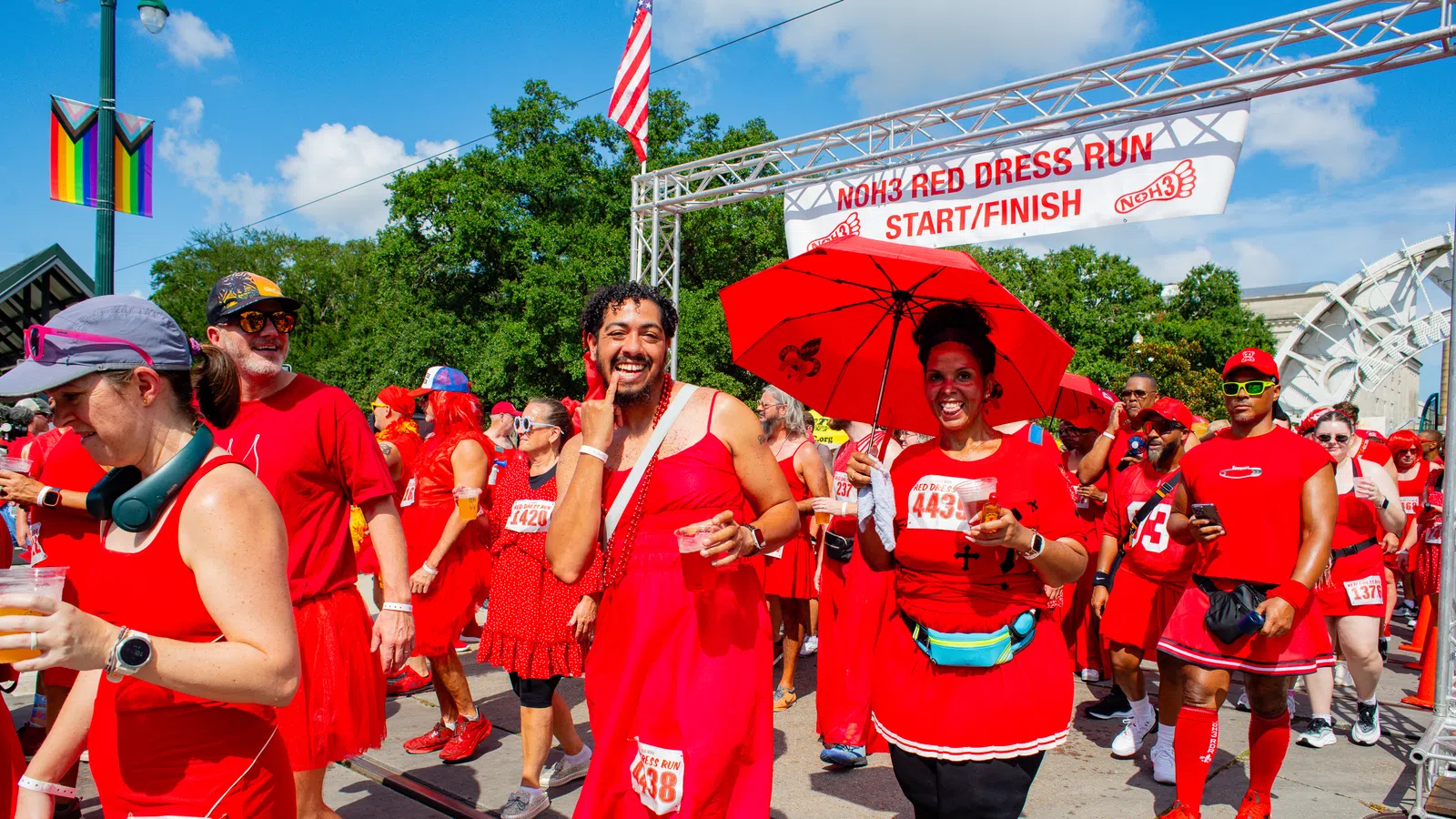 Participants in red dresses enjoy the NOH3 Red Dress Run at the start/finish line under a sunny sky.