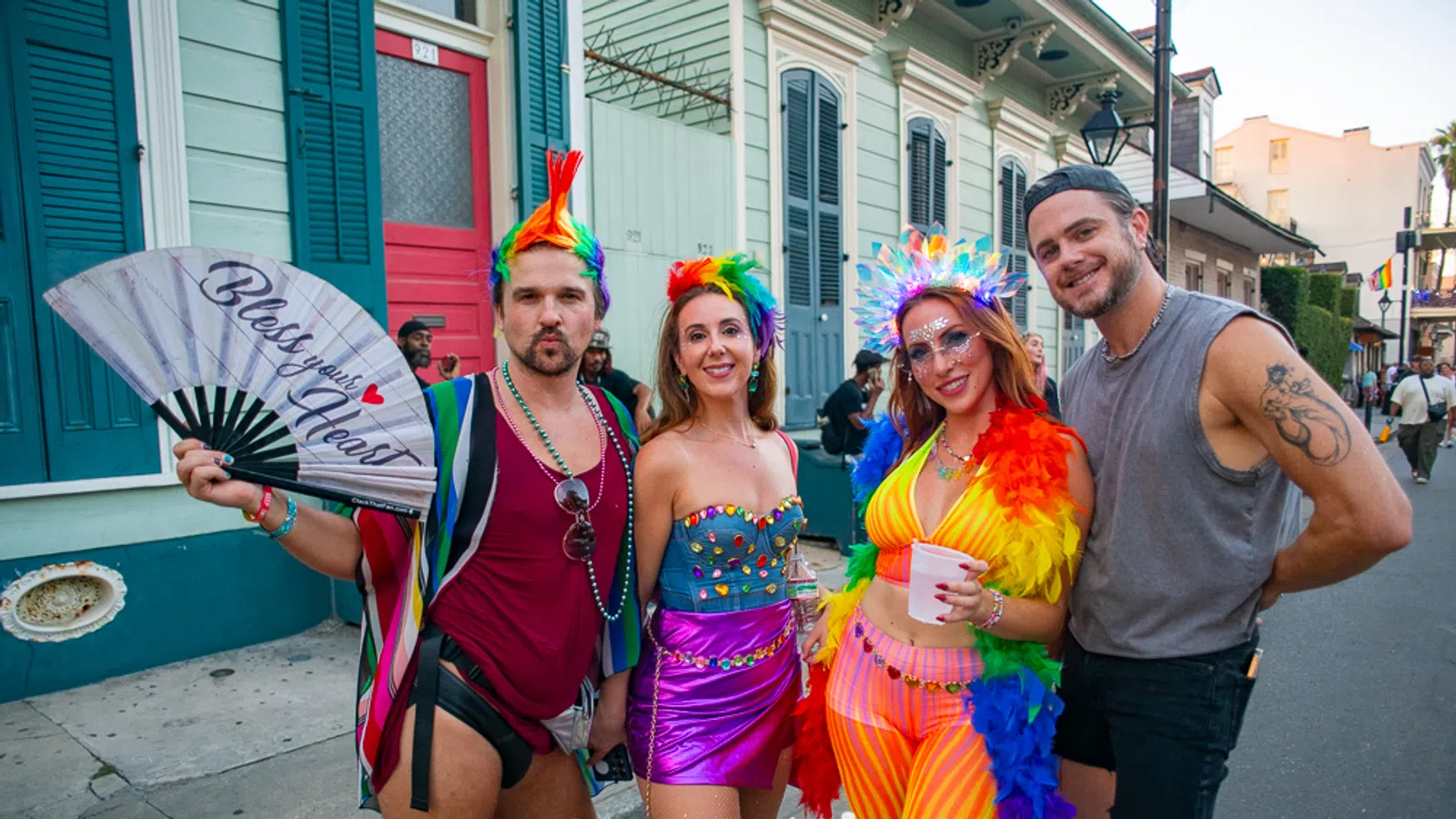 Four colorful, lively people in festive rainbow outfits posing on a New Orleans street during a celebration.
