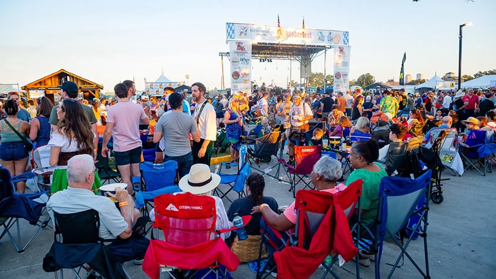 Crowd enjoying an outdoor concert event with people seated in folding chairs and a stage in the background